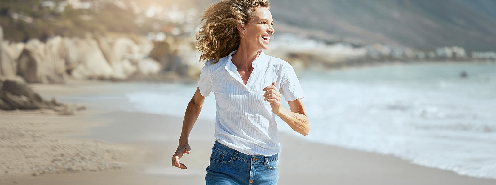 Woman joyfully running on beach shore.