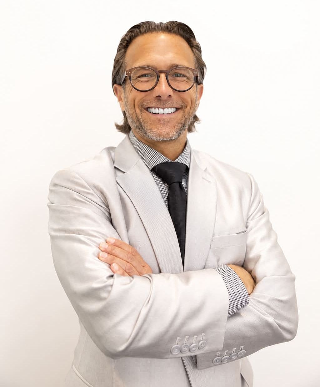 Smiling man in a light suit, arms crossed.
