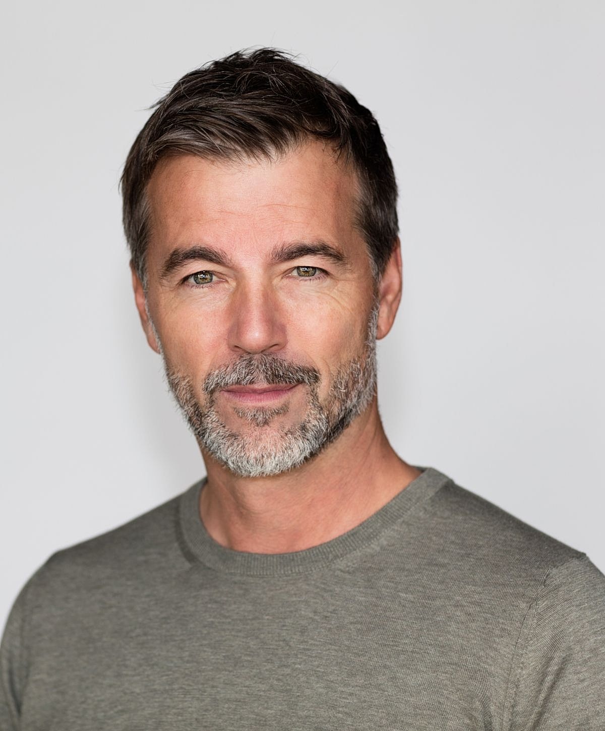 Man with beard smiling in a grey shirt.