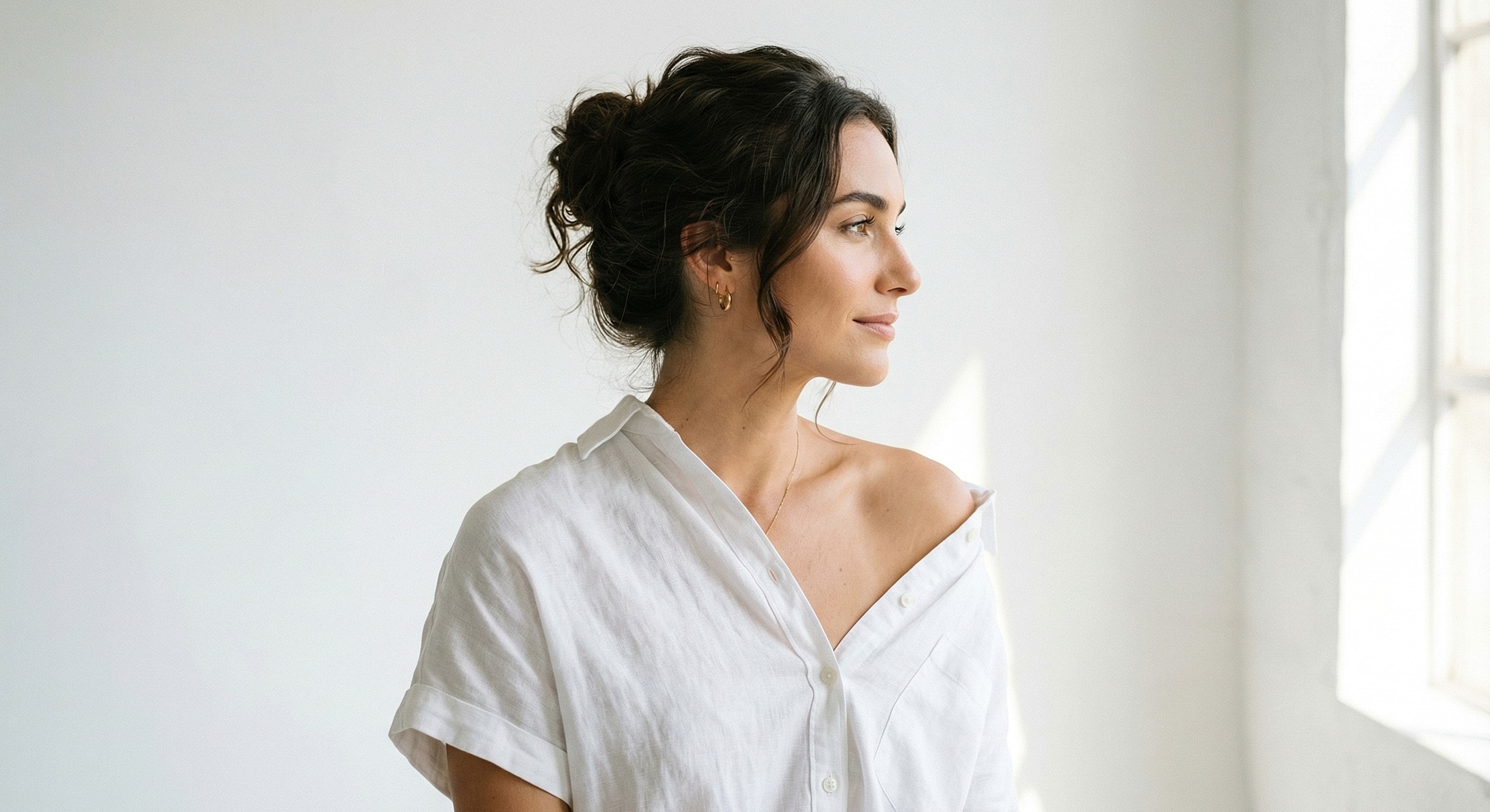 Woman in white shirt looking out a window.