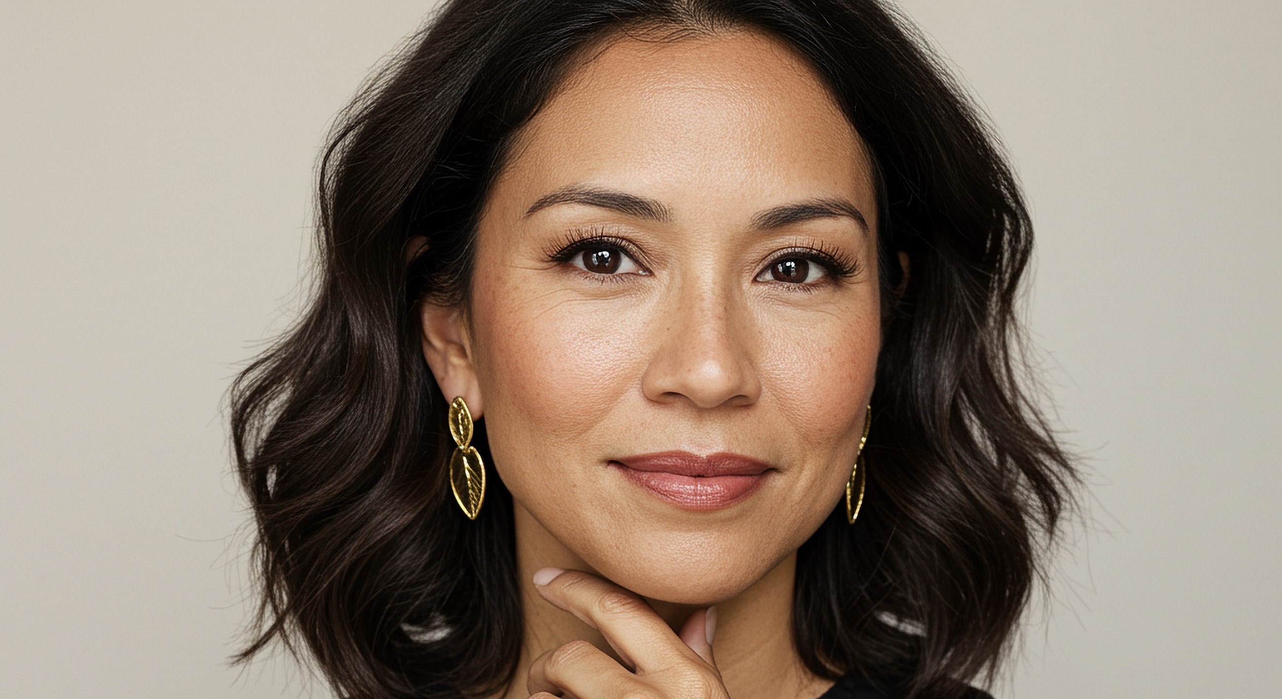 Woman with wavy hair and gold earrings, smiling.